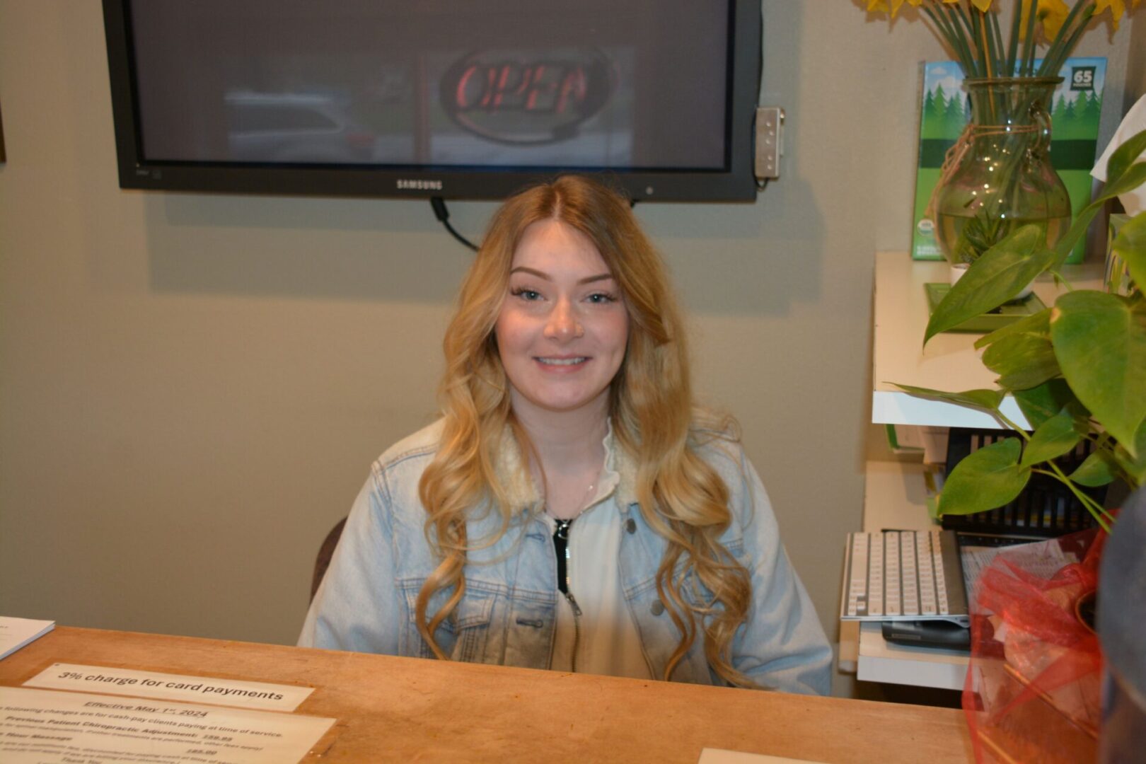 A smiling young woman with long blonde hair sitting at a desk.