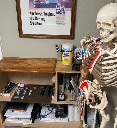 A human skeleton model stands near a cluttered desk with office supplies.