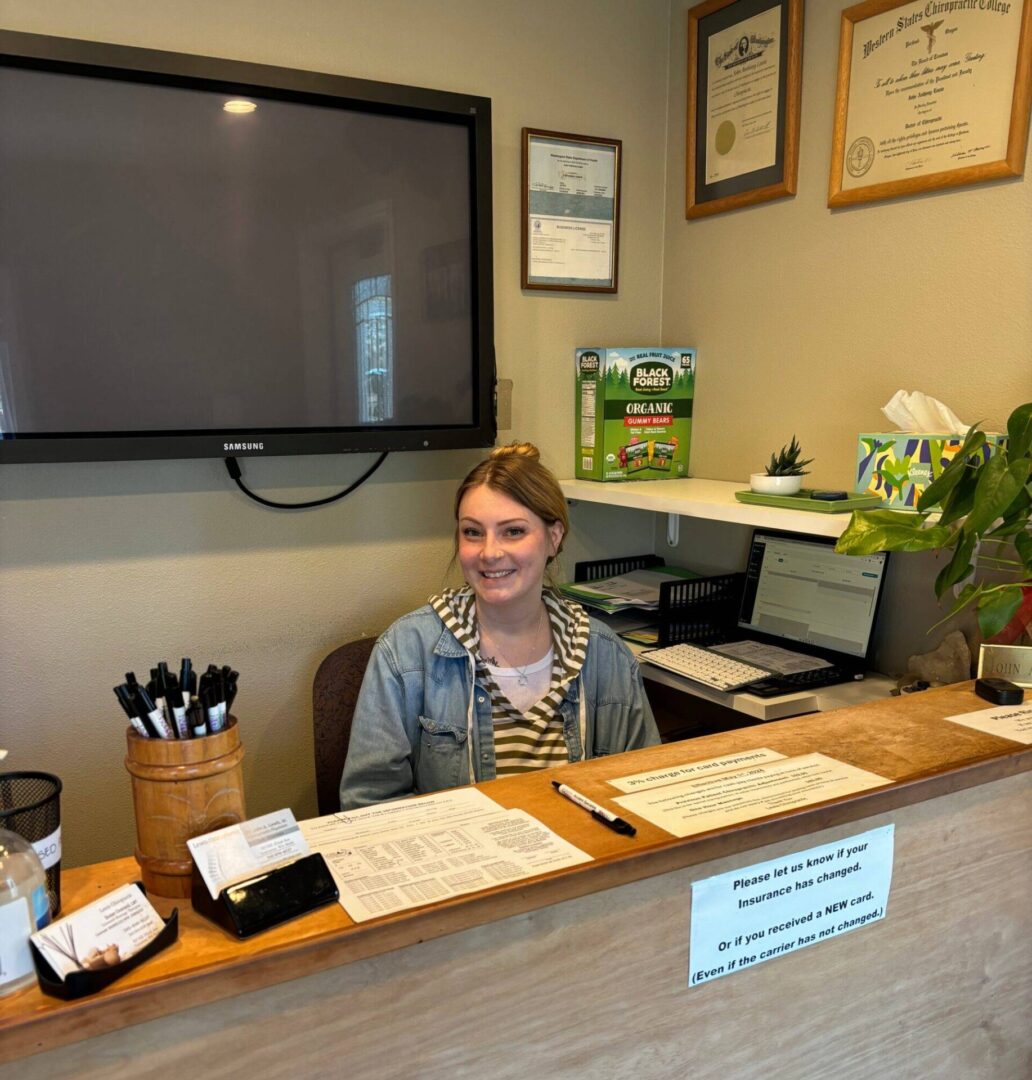 Receptionist sitting behind a cozy office desk with certificates on the wall.