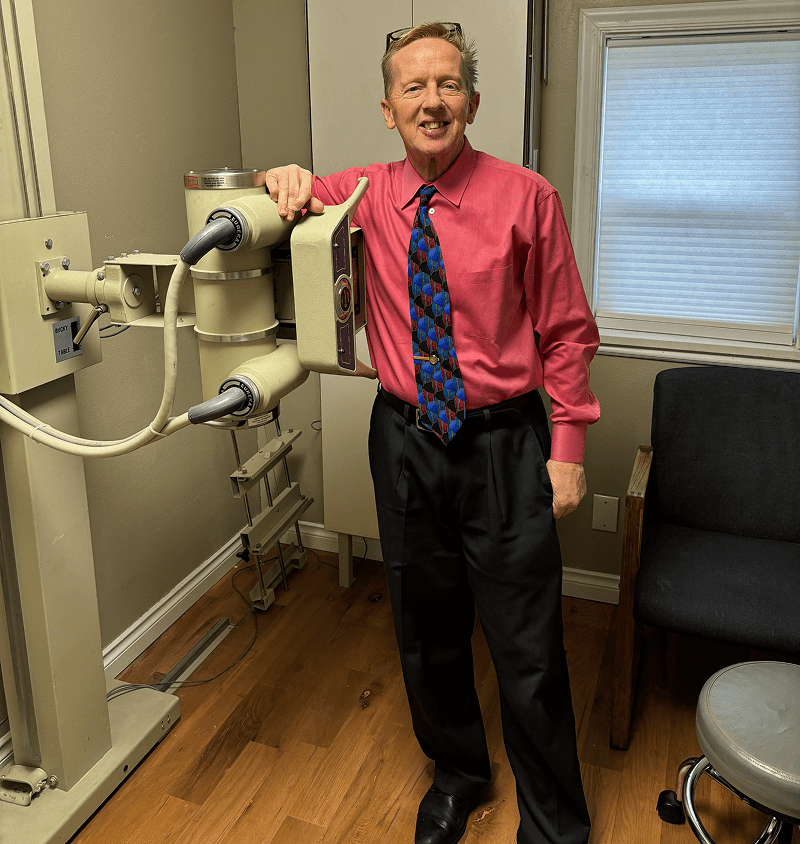 Man in a bright pink shirt stands next to medical imaging equipment.